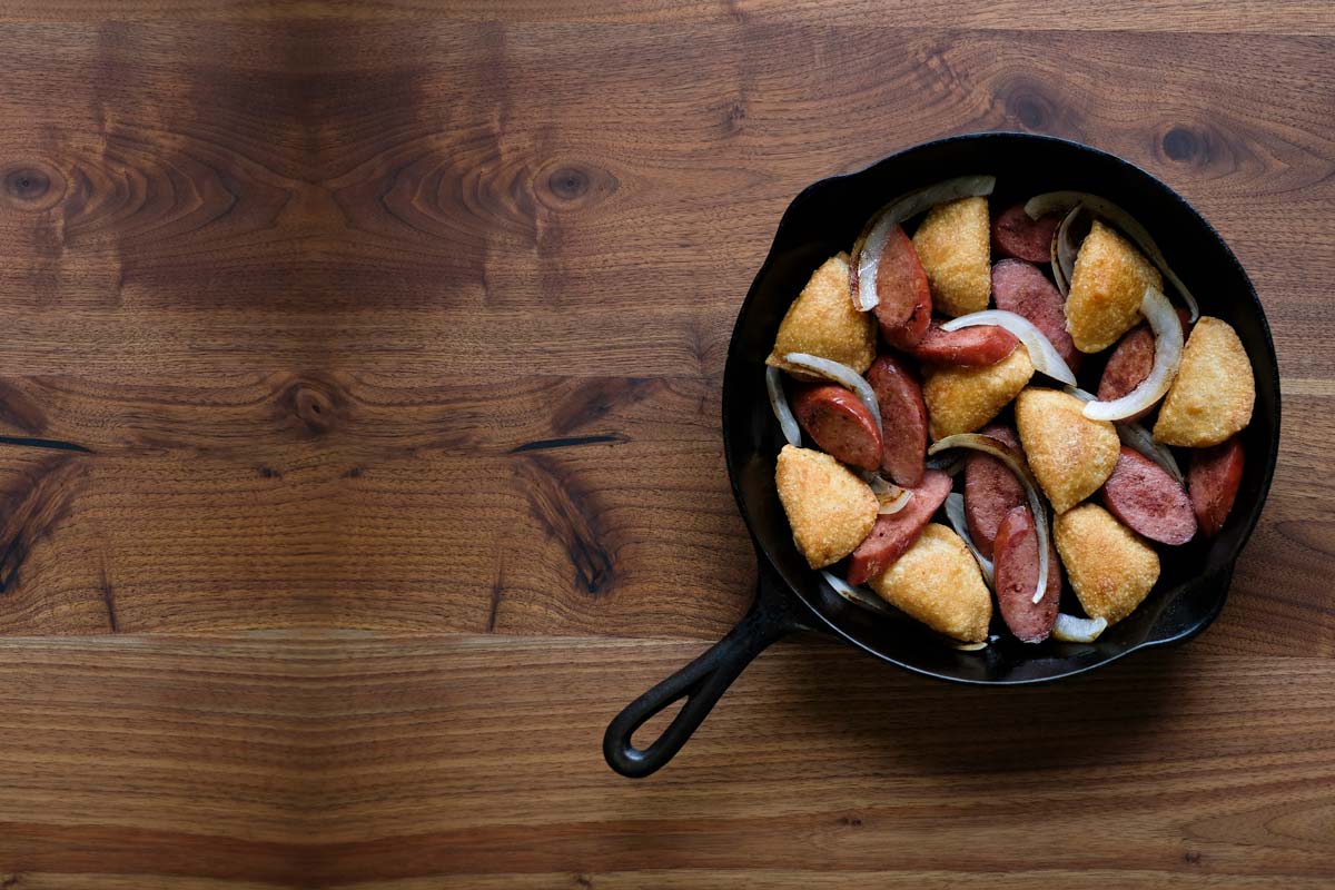 A cast Iron skillet with fried perogies, sausage, and onions.