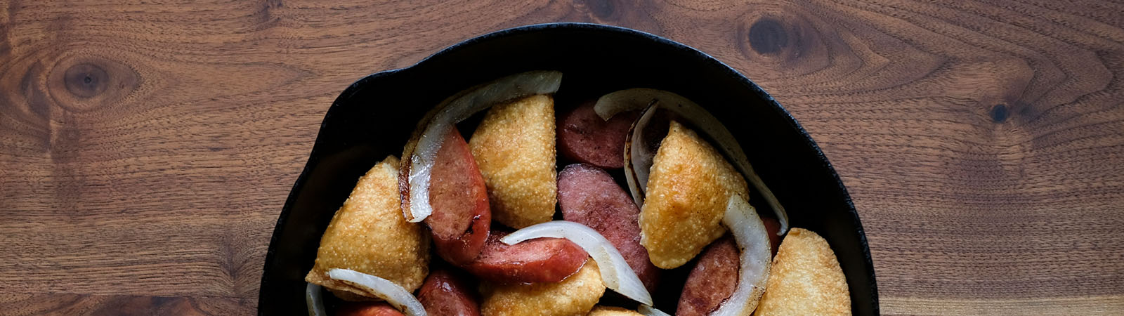 Fried Pierogies, Garlic Sausage, and onions in a cast iron skillet